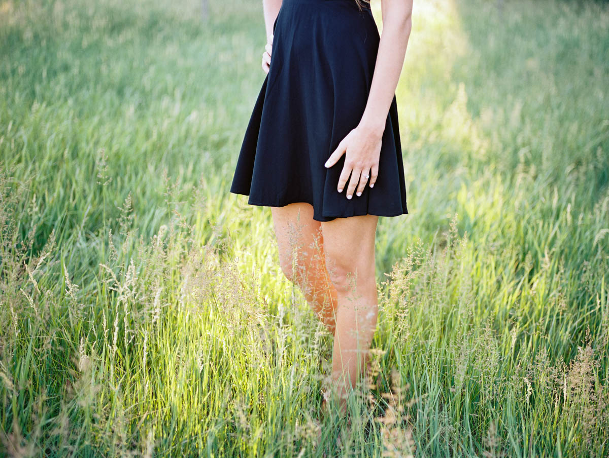 bottom half of a woman standing in a field, showing off her engagement ring
